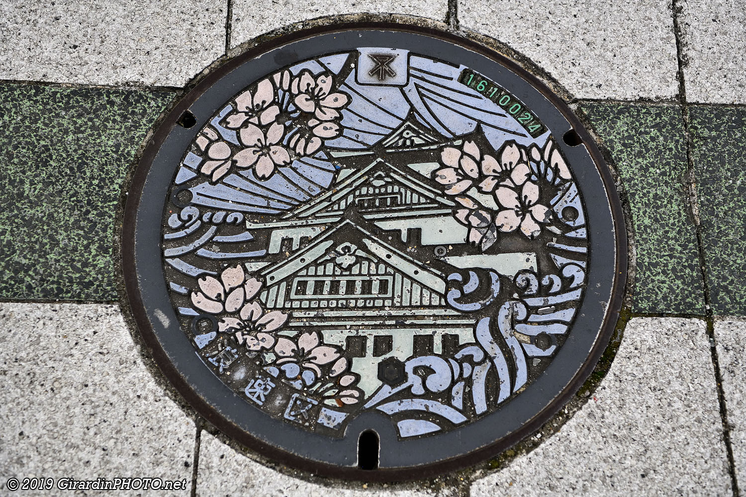 Grille d’égout avec le château d’Osaka et les fleurs de cerisiers, emblème de la ville